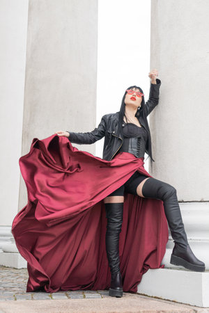 Woman with long hair, perfect figure, sexy. she is in a satin, long red skirt, leather jackets. Posing in the city at the tall ancient columnsの写真素材