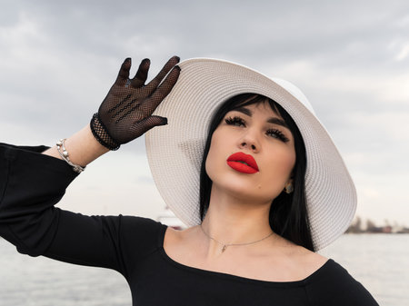 A woman with a perfect figure in a black dress, on the pier in a white hat. looking at the cameraの写真素材