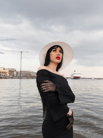 A woman with a perfect figure in a black dress, on the pier in a white hat. looking at the cameraの写真素材