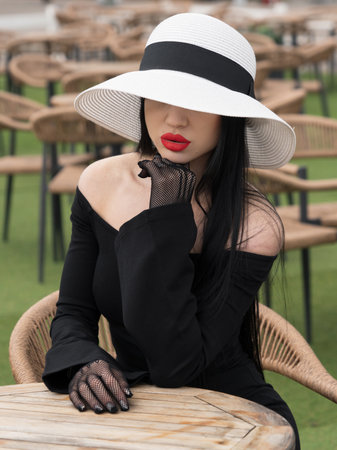 A woman in a black dress, at a table in a summer cafe in a white hat. Oneの写真素材