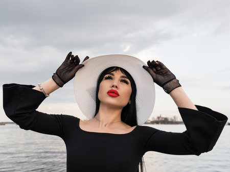 A woman with a perfect figure in a black dress, on the pier in a white hat. looking at the cameraの写真素材