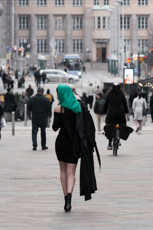 A woman with a perfect figure and red lips in a short black dress, a bright scarf on her head. Posing in the cityの写真素材