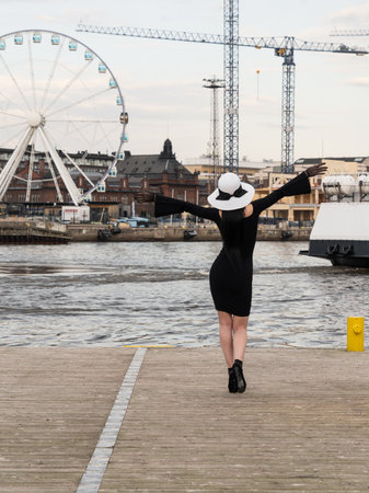 A woman with a perfect figure in a short black dress, on the pier in a white hat. Meets the ferry, waving his handsの写真素材