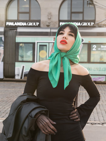 Helsinki. Finland. 25.04.2023. A woman with a perfect figure and red lips in a short black dress, a bright scarf on her head. Posing in the cityの写真素材