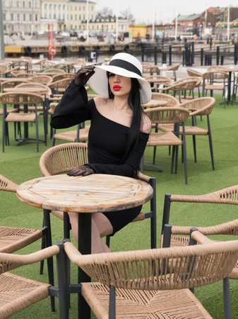 A woman in a black dress, at a table in a summer cafe in a white hat. Oneの写真素材