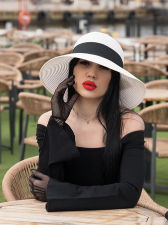 A woman in a black dress, at a table in a summer cafe in a white hat. Oneの写真素材