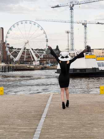 A woman with a perfect figure in a short black dress, on the pier in a white hat. Meets the ferry, waving his handsの写真素材