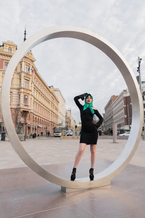 Helsinki. Finland. 25.04.2023. A woman with a perfect figure and red lips in a short black dress, a bright scarf on her head. Posing in the cityの写真素材