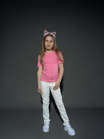 A cheerful but serious teenage girl with long, blond hair in a pink T-shirt and jeans posing in the studio. On a gray background. freedom conceptの写真素材