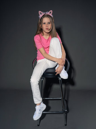 A cheerful but serious teenage girl with long, blond hair in a pink T-shirt and jeans posing in the studio. On a gray background. freedom conceptの写真素材