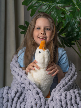 Cheerful, teenage girl with long hair, wrapped in a plaid with a large knit. she has a toy goose in her handsの写真素材