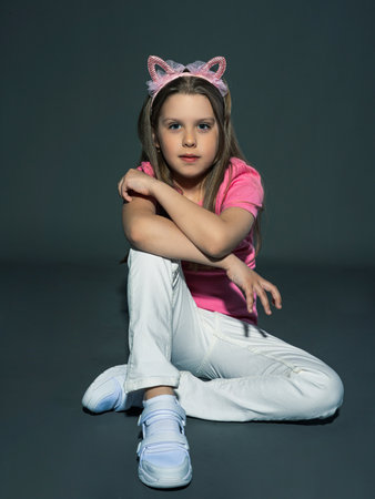 A cheerful but serious teenage girl with long, blond hair in a pink T-shirt and jeans posing in the studio. On a gray background. freedom conceptの写真素材