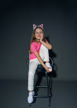 A cheerful but serious teenage girl with long, blond hair in a pink T-shirt and jeans posing in the studio. On a gray background. freedom conceptの写真素材