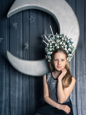 user A girl with long, beautiful hair in a large royal crown of flowers, she is in a photo studio against the backdrop of a huge moon. Looks straight into the cameraの写真素材