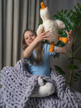 Cheerful, teenage girl with long hair, wrapped in a plaid with a large knit. she has a toy goose in her handsの写真素材