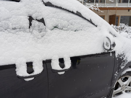 A cropped image of a black car covered in a thick layer of snow. The door handles and windows are partially visible beneath the snow, emphasizing the frosty and wintry atmosphere.の写真素材