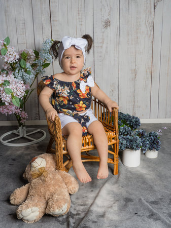 Baby sitting in a straw chair with a plush bear beside. Surrounded by flowers, the scene captures a cozy and sweet moment.の写真素材