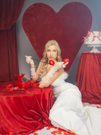 Beautiful blonde girl in a red dress with a telephone in the shape of a heartの写真素材