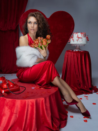 Beautiful girl in a red dress with a bouquet of tulips sitting on the floorの写真素材