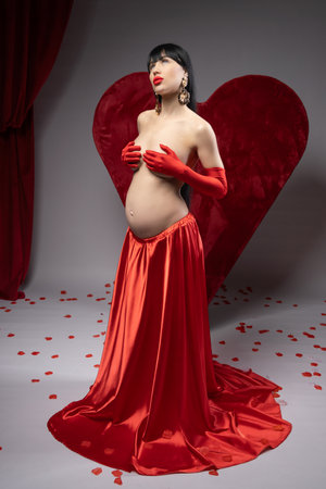 Pregnant woman in red dress and gloves sitting on the heartの写真素材
