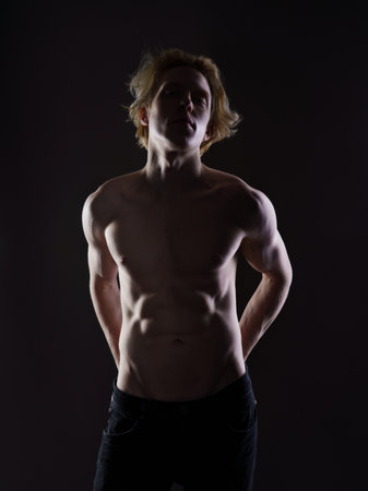 Portrait of a shirtless young man with blond hair on a dark background