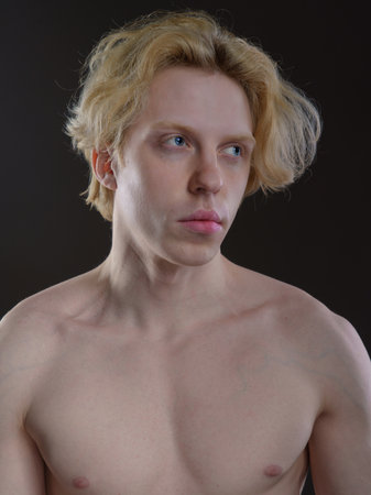 Portrait of a young man with blond hair on a dark backgroundの写真素材