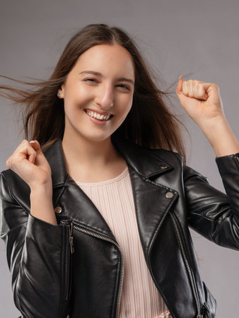 Portrait of a beautiful young woman in a leather jacket on a gray backgroundの写真素材