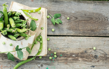 green peas on rustic wooden background in old metal mug and old books