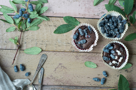 Honeysuckle berry and cup cakes with green leaves on a wooden table. Beautiful still life photoの写真素材