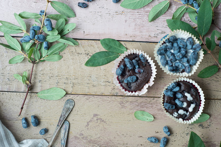 Honeysuckle berry and cup cakes with green leaves on a wooden table. Beautiful still life photoの写真素材