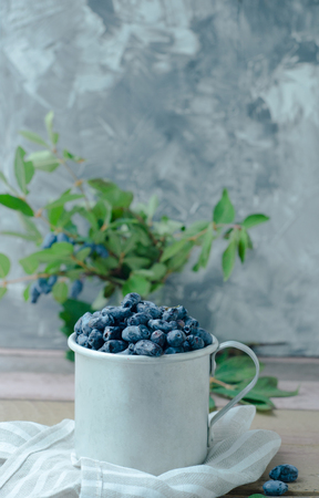 Honeysuckle berry in metal cup with green leaves on a wooden table. Beautiful still life photoの写真素材