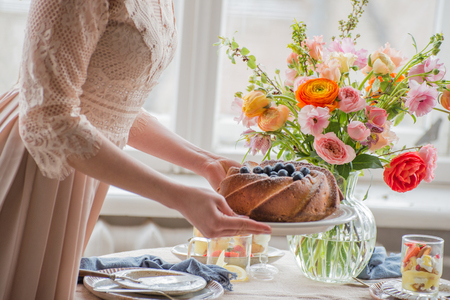 Tea time, Beautiful woman hands with tea pot, beautiful flower bouquet, cake, arranged on tableの写真素材