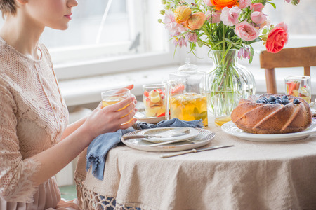 Tea time, Beautiful woman hands with tea pot, beautiful flower bouquet, cake, arranged on tableの写真素材
