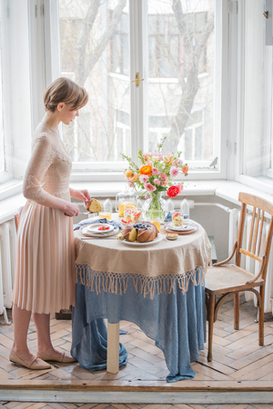 Tea time, Beautiful woman with tea pot, beautiful flower bouquet, cake, arranged on tableの写真素材