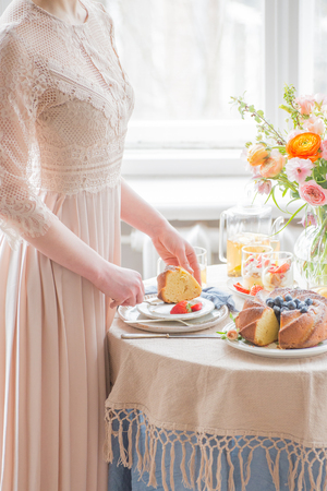 Tea time, Beautiful woman hands with tea pot, beautiful flower bouquet, cake, arranged on tableの写真素材