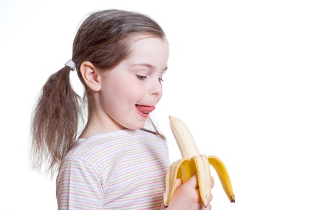 The happy little girl licks lips and wants to bite off bananaの写真素材