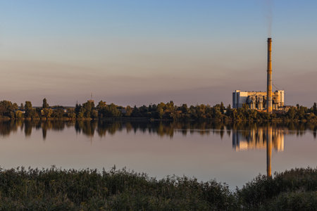 Waste processing plants chimneys emit smoke at sunset on the lake. Despite generating energy, it leads to air and environmental pollution.の写真素材