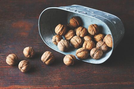 Unpeeled walnuts beautifully falling out of a grey metallic bowlの写真素材