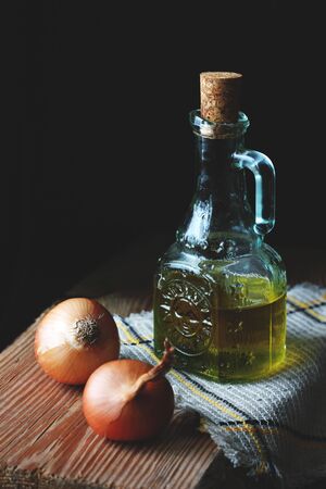A Glass Bottle With Olive Oil With Two Onions Lying Around On the Piece Of Woodの写真素材