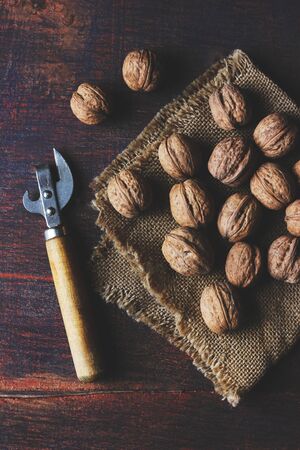 dark and moody still life photo of unpeeled walnuts lying on a napkin with a nutcracker lying around...