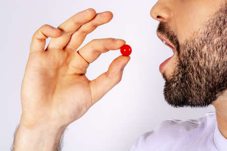Man putting red pill in his mouth. Taking medications in motion. Man taking pills close up on white background.の写真素材