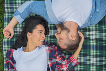 Love couple lie and relax on a blanket in the park. Attractive guy and beautiful young girl romantic pastime. Love sight and beginning of relationshipの写真素材