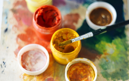 Top view of one paint brush and several open jars of gouache of different colors standing on the paletteの写真素材
