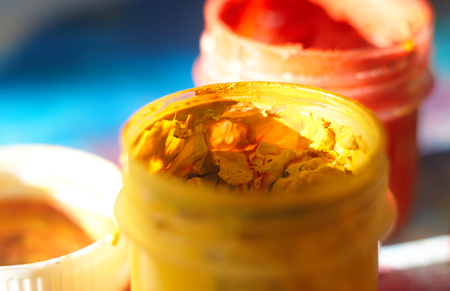 Two open jars with red and yellow gouache and a lid from them on a bright blue backgroundの写真素材