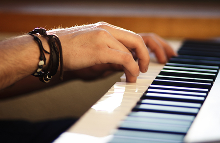 On the keyboard instrument, which is illuminated by weak sunlight, men's hands press the keys,...