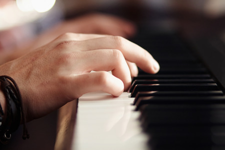 Hands, with a bracelet of ropes and beads, play on a modern musical synthesizer with black and white keysの写真素材