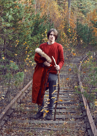 A handsome guy in red clothes stands on an abandoned railway track in the middle of the autumn forestの写真素材