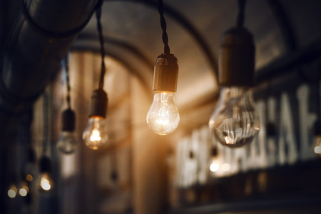 Glass light bulbs hanging on the wires on the roof near the cafe, glow brightly in the darkness of the nightの写真素材