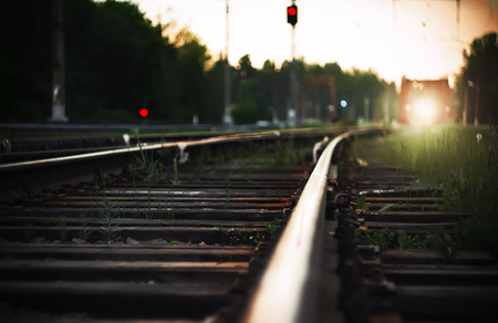 Bright light from the headlights of the approaching train, which rides on rails with wooden sleepers in the countryside. Next to the railway tracks are red traffic lights, warning of danger.の写真素材