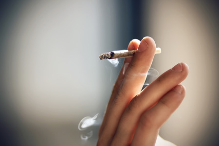 Human elegantly holds in the fingers of a hand Smoking a cigarette, illuminated of natural bright...